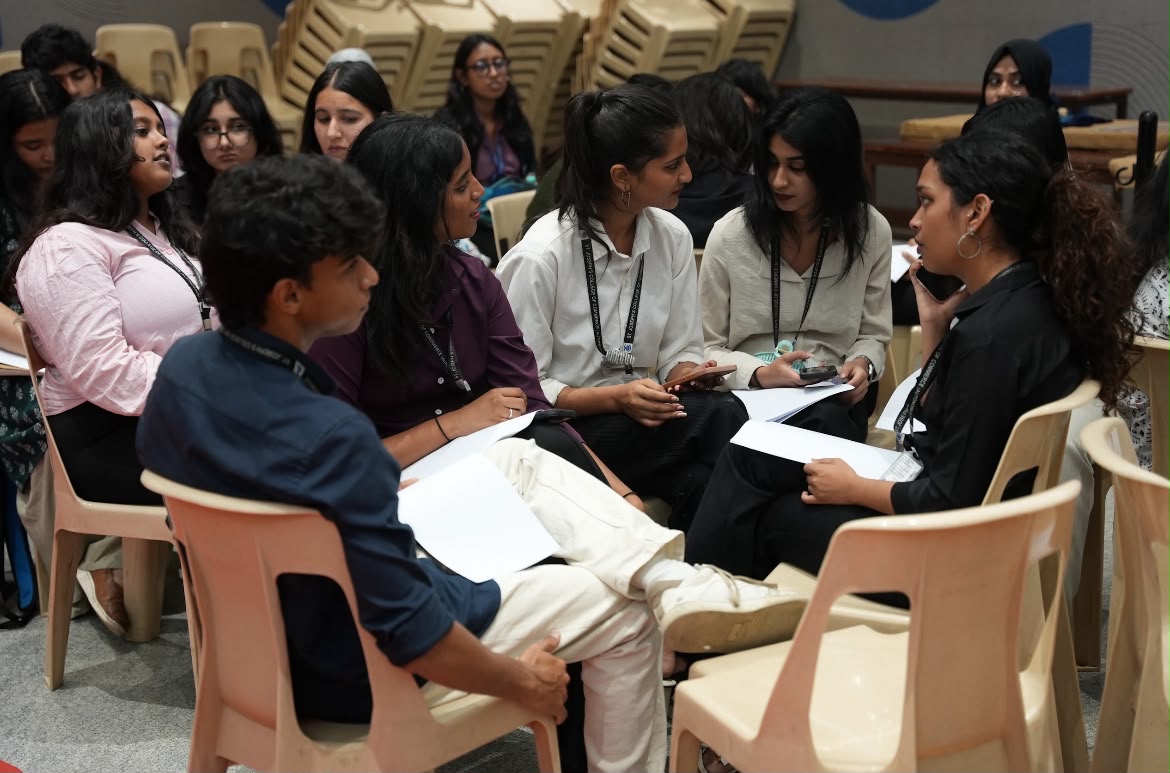 Students in a circle discussing with papers in hand