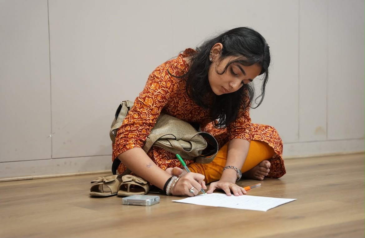 Student writing on a sheet of paper while seated on the floor